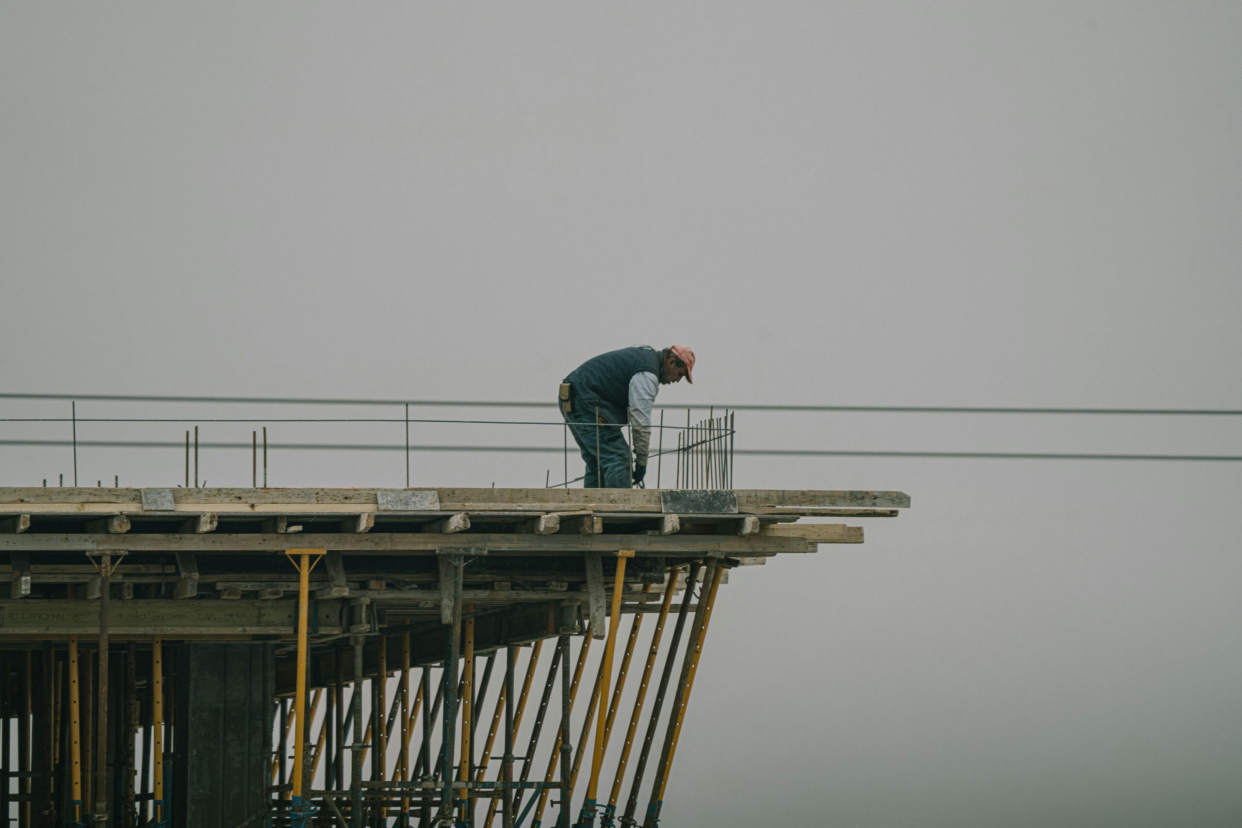 A construction worker bends over rebar on a high framework under a foggy sky in Denizli, Türkiye.